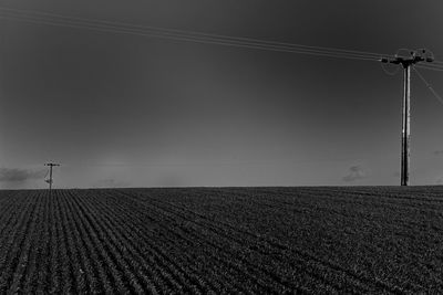 Electricity pylons on agricultural field against sky