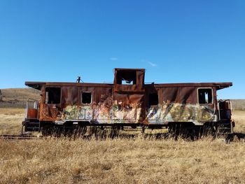 Abandoned train on field against clear blue sky