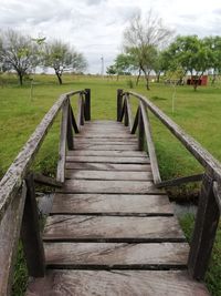Empty footpath amidst field against sky