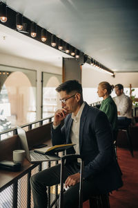 Businessman with hand on chin looking at laptop in hotel