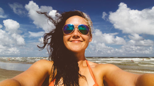 Portrait of smiling beautiful woman at beach against sky