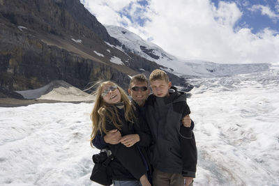 Father standing with children at athabasca glacier in jasper national park against sky
