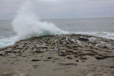 Waves splashing on shore at beach against sky