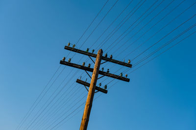 Low angle view of electricity pylon against blue sky