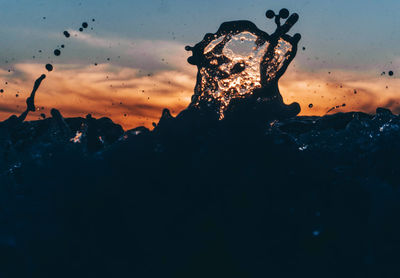 Close-up of silhouette water splashing against sky during sunset