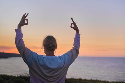 Optical illusion of man with arms raised against sea during sunset