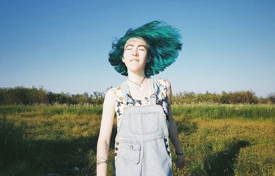 Young woman standing on field against sky