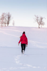 Rear view of woman walking on snow covered field