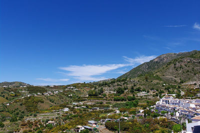 Scenic view of town by mountains against blue sky