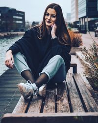 Young woman sitting on bench by canal in city