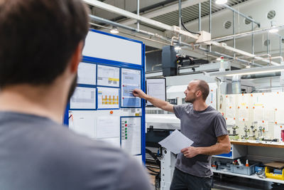 Maintenance engineer discussing over business plan while standing with coworker at factory