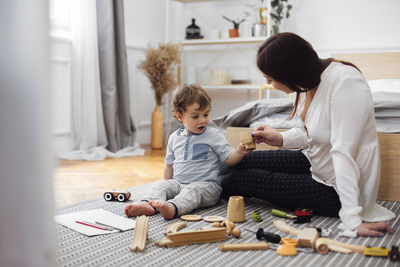 Mother and baby boy toasting toy teacups while sitting on rug at home