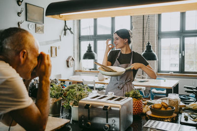 Male photographer taking picture of female chef gesturing while holding cooking pan at studio kitchen