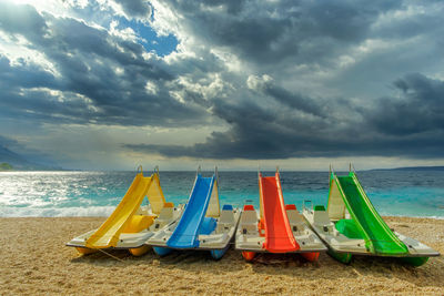 Pedal boats on beach against cloudy sky