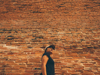 Low angle view of woman standing by brick wall