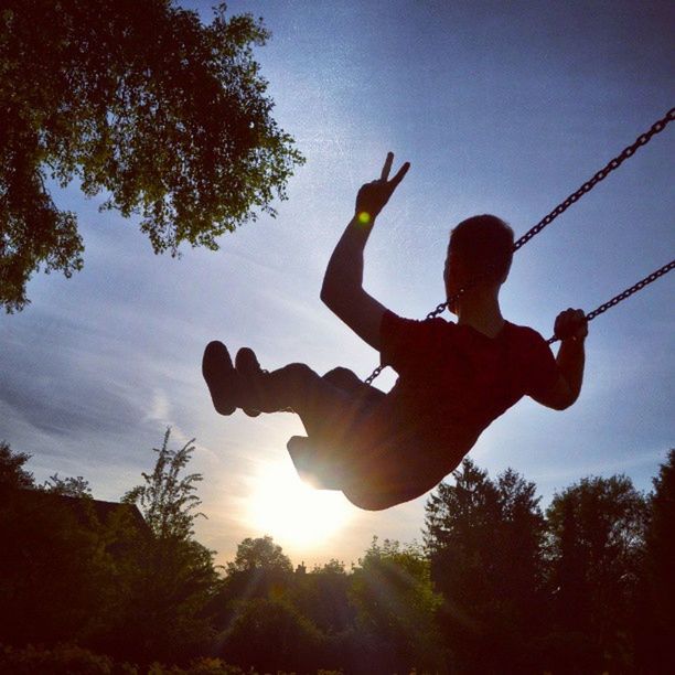 leisure activity, lifestyles, low angle view, silhouette, tree, enjoyment, sky, fun, men, arms raised, holding, playing, skill, technology, sunlight, sun, photographing, jumping
