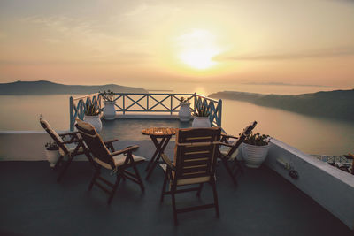 Chairs and table at building terrace against sea and sky during sunset