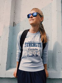 Young woman wearing sunglasses standing against wall