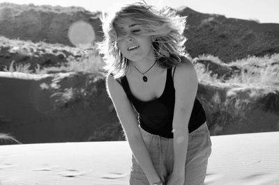 Portrait of young woman standing against sand dune