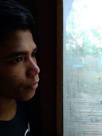 Portrait of young man looking through window at home