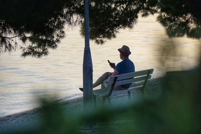 Rear view of man sitting on chair at lake