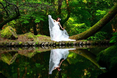 Woman standing by plants in lake against trees in forest