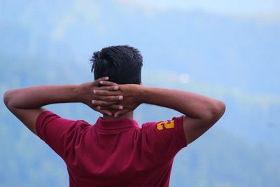 Rear view of man with hands behind head standing outdoors