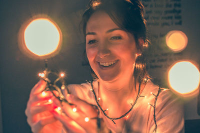 Portrait of smiling young woman standing against illuminated lights at night