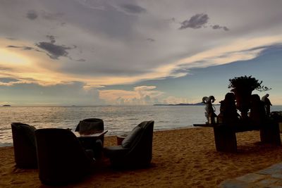 People sitting on chair at beach against sky during sunset