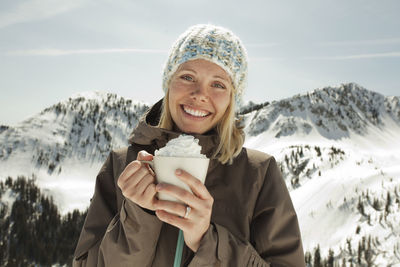 Portrait of woman holding whipped cream while standing against snowcapped mountain