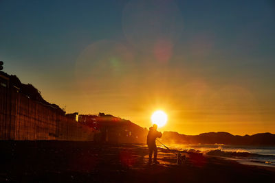 Silhouette man on beach against sky during sunset