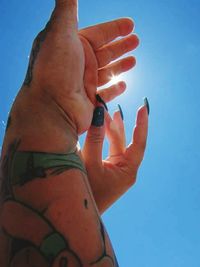 Low angle view of cropped hand against blue sky