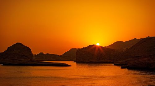 Scenic view of rock on sea against orange sky