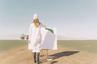 Young woman on dry field, painting canvas with green paint