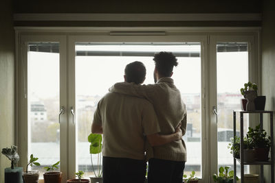 Homosexual couple standing with arms around and looking through window