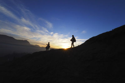 Silhouette people walking on mountain against sky during sunset