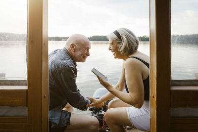 Happy senior couple with smart phone sitting on houseboat