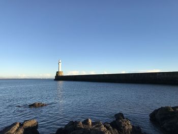 Lighthouse by sea against clear sky