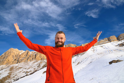 A bearded attractive caucasian man in a red sweater and jeans joyfully throws up his hands winter 