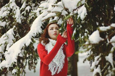 Redhead beautiful woman in red sweater and white gloves walking in the frozen winter forest.