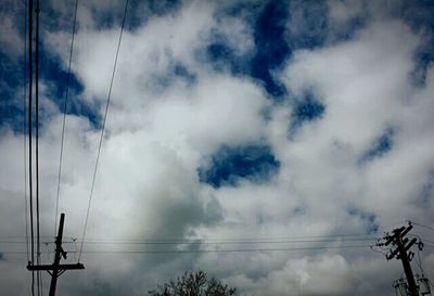 Low angle view of electricity pylon against cloudy sky