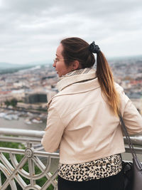 Rear view of woman looking away while standing by railing against sky