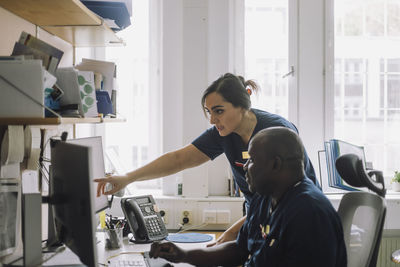 Female nurse pointing over computer while discussing with colleague at hospital