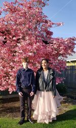 Full length of friends standing against pink flowers in park