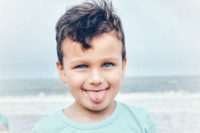 Close-up portrait of boy sticking out tongue at beach against sky