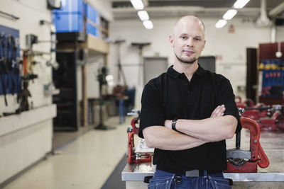 Portrait of confident auto mechanic teacher standing arms crossed in workshop