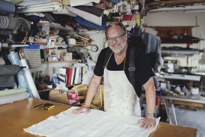 Portrait of smiling male owner standing with fabric at workbench