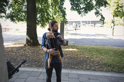 Mid adult father carrying baby in carrier on sidewalk