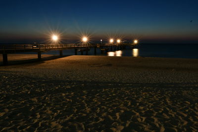 Illuminated street lights on beach against sky at night