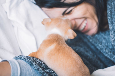 Close-up of smiling woman playing with puppy while lying on bed